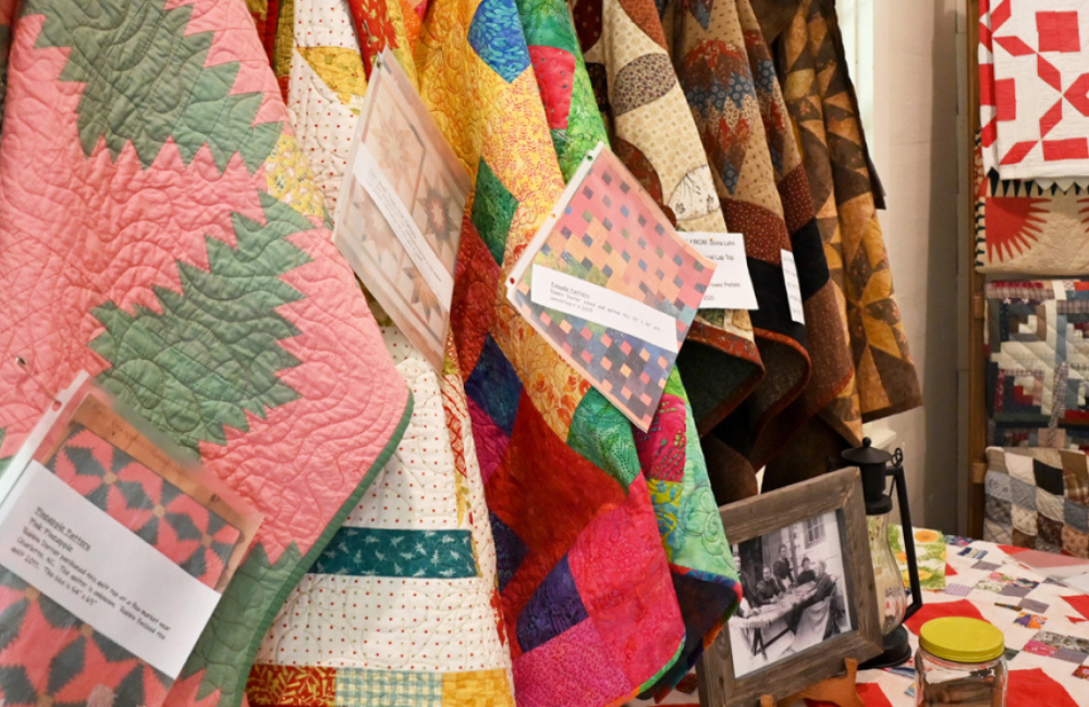 Several colorful handmade quilts hanging together for sale