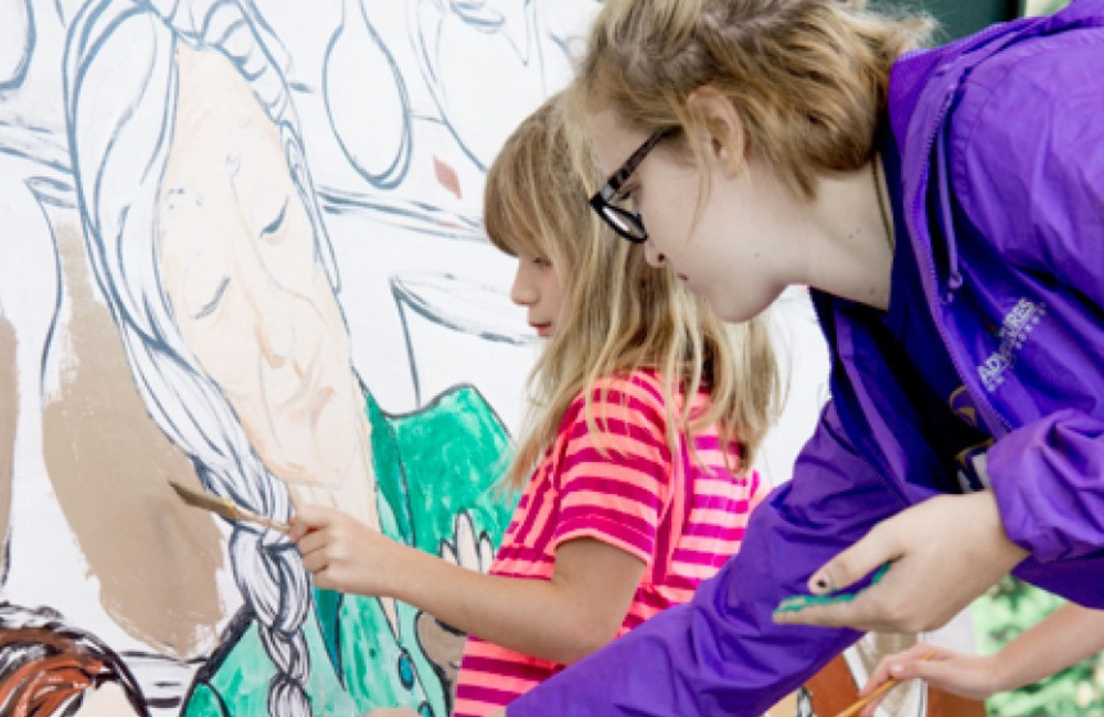 Teen and younger children painting a mural