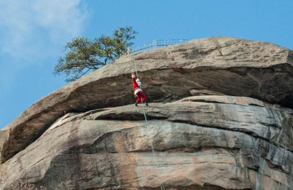 Santa using a rope and harness to climb to the top of Chimney Rock