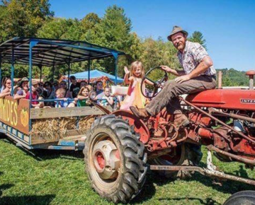 Man on a tractor pulling a hay wagon full of smiling people